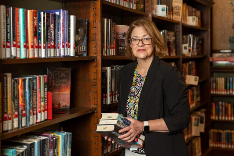 Bev Clarkson at the Pittsburg Public Library posing in front of books.